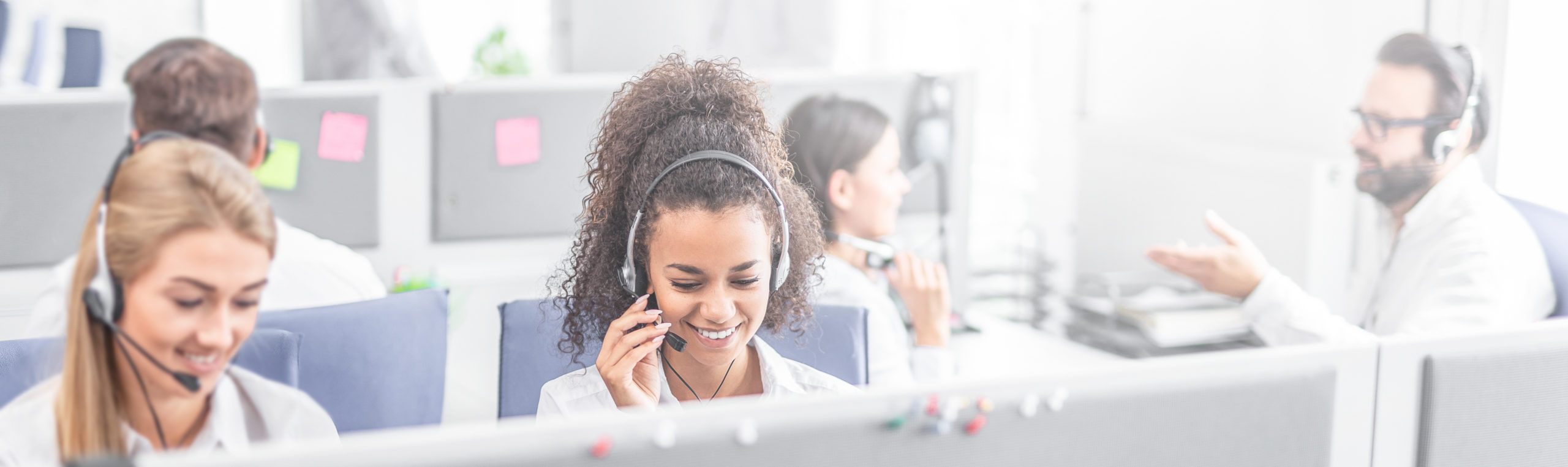 Call center worker accompanied by her team. Smiling customer support operator at work. Young employee working with a headset.