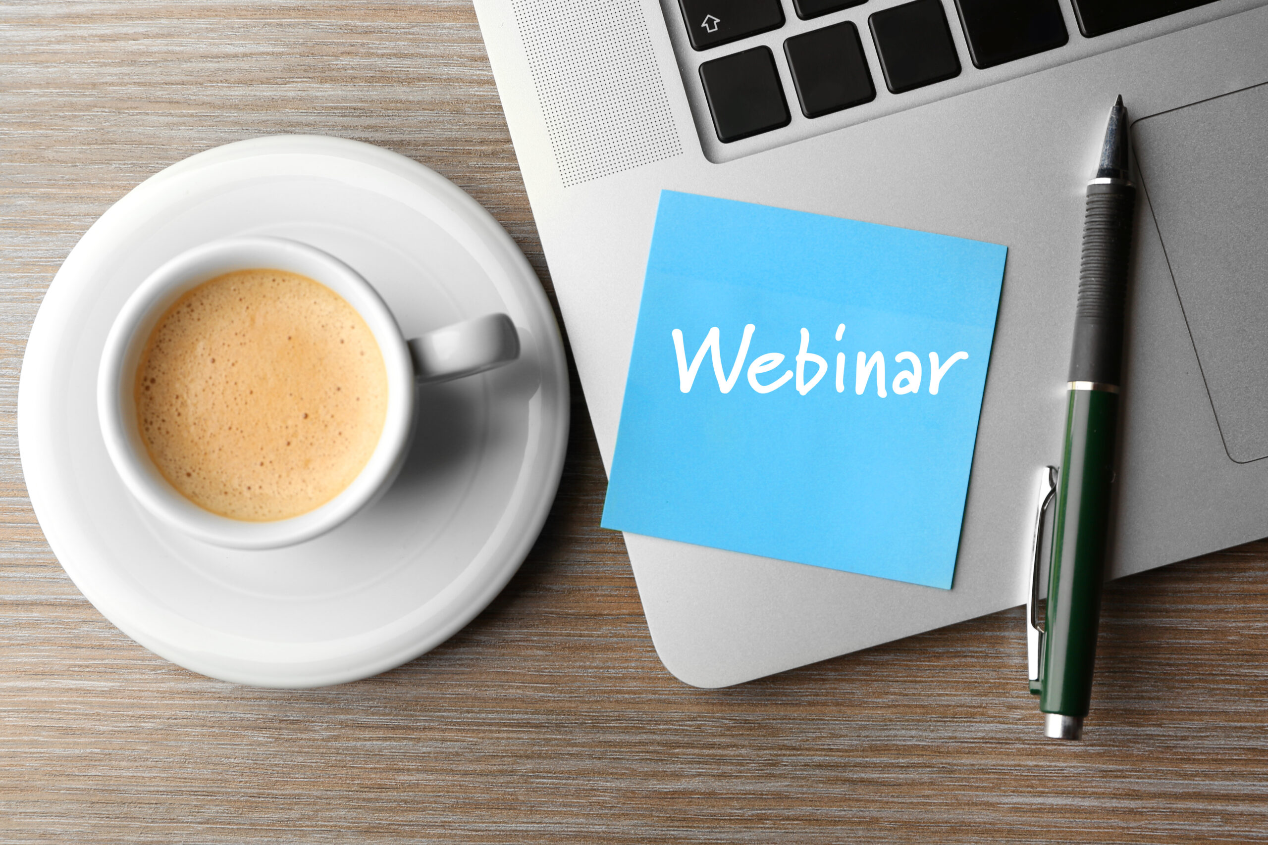 Webinar written on sticky note, laptop and cup of coffee on table, top view